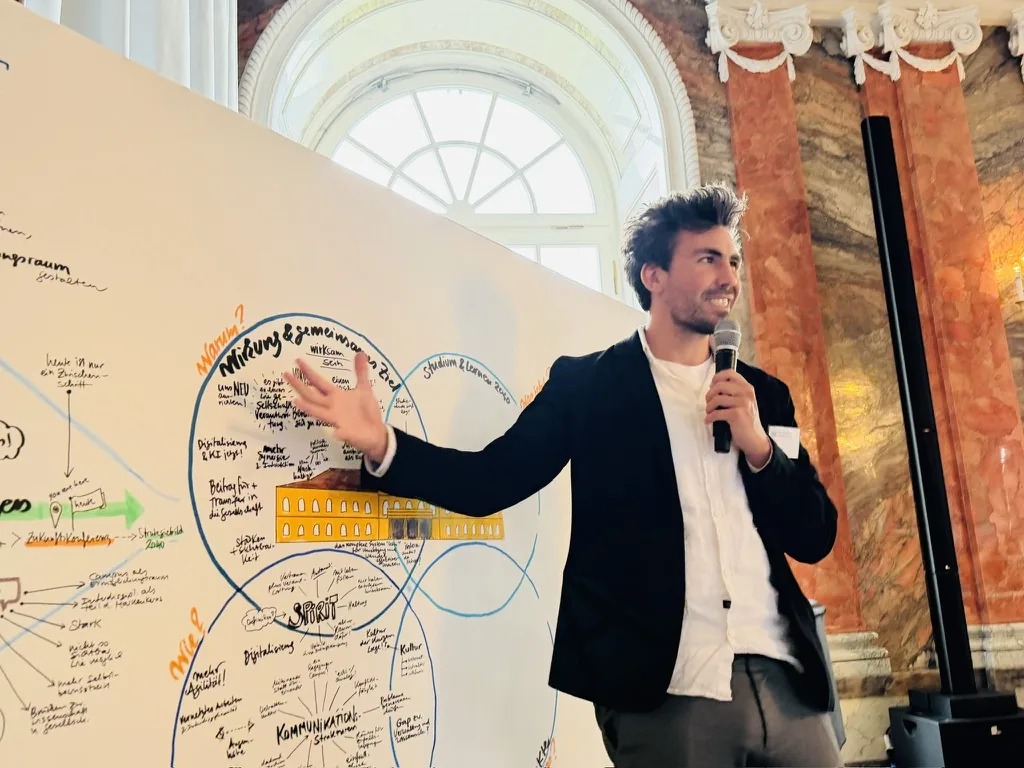 Robin Hotz moderiert mit Mikrofon auf einer Konferenzbühne