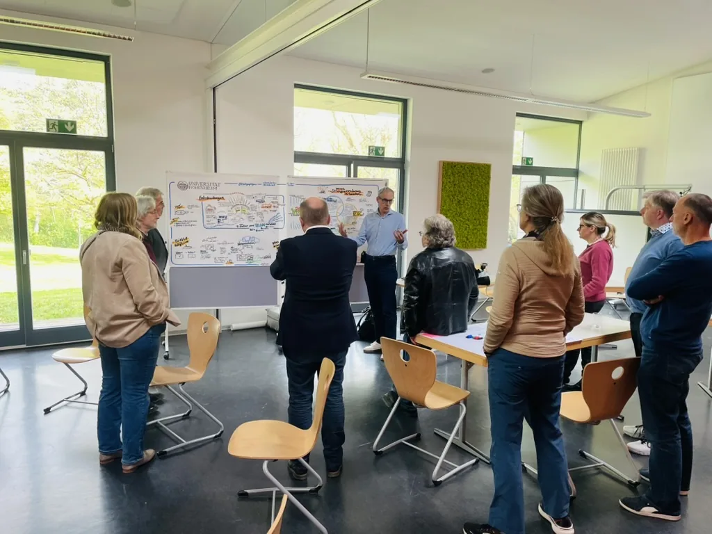 Teilnehmende tauschen sich in kleinen Gruppen vor einer Visualisierung aus